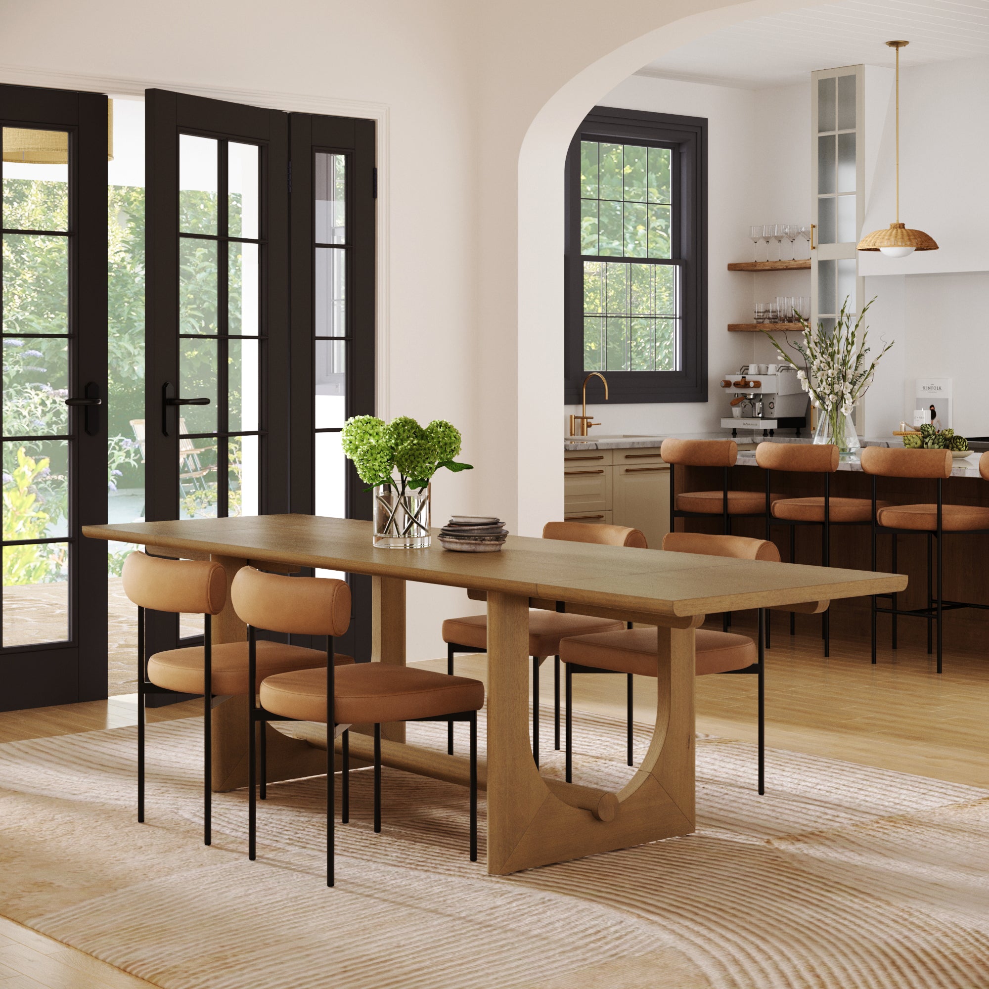 A modern dining room showcases the Nathan James Extendable Dining Table Set with a solid wood table and four faux leather chairs. Large windows brighten the space, with open kitchen shelves and bar stools in the background.