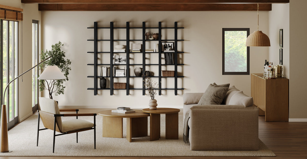 A living room with a large black wall-mounted shelving unit, a neutral sofa, a wooden armchair, and two circular coffee tables.
