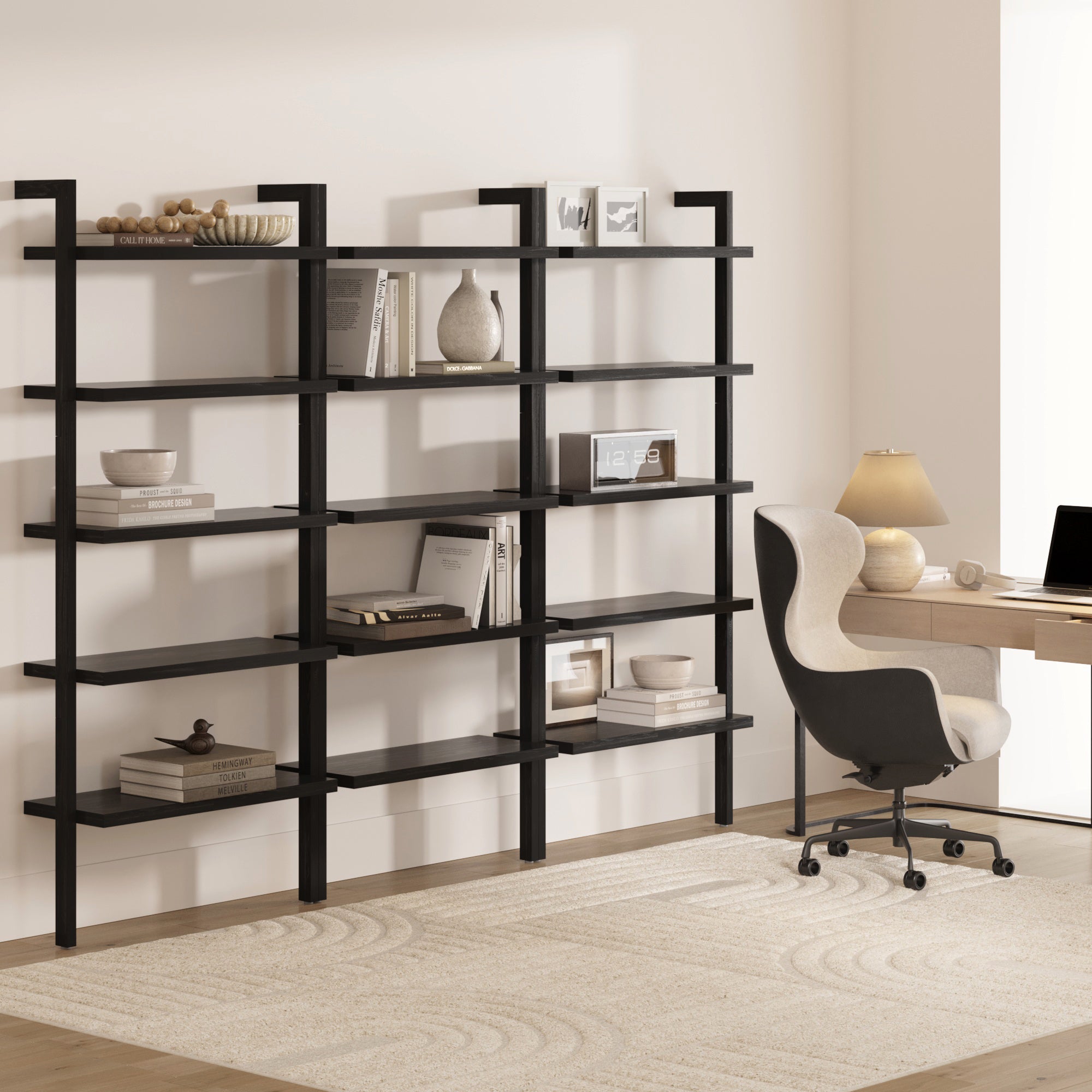 A modern home office showcases Nathan James Wood 5 Tier Wall Mounted Bookshelves in black oak (set of 3) with books and decor, a beige desk with lamp, and an ergonomic chair on a light rug in a neutral-toned room.