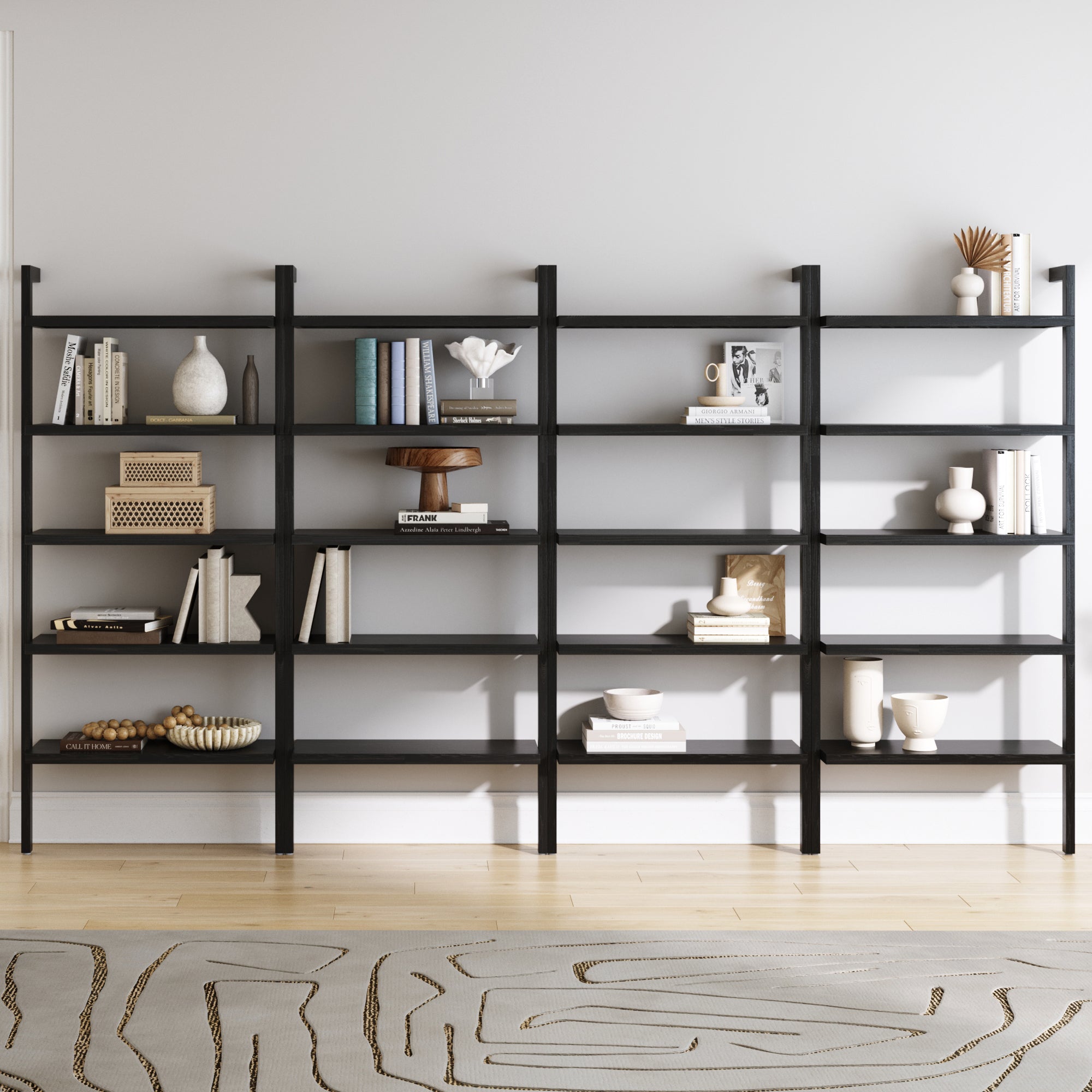 The Nathan James Wood 5 Tier Wall Mounted Bookshelf in Black Oak (Set of 4) is displayed against a light gray wall, filled with books, vases, and baskets. A patterned rug lies on the light wood floor in front of the shelves.