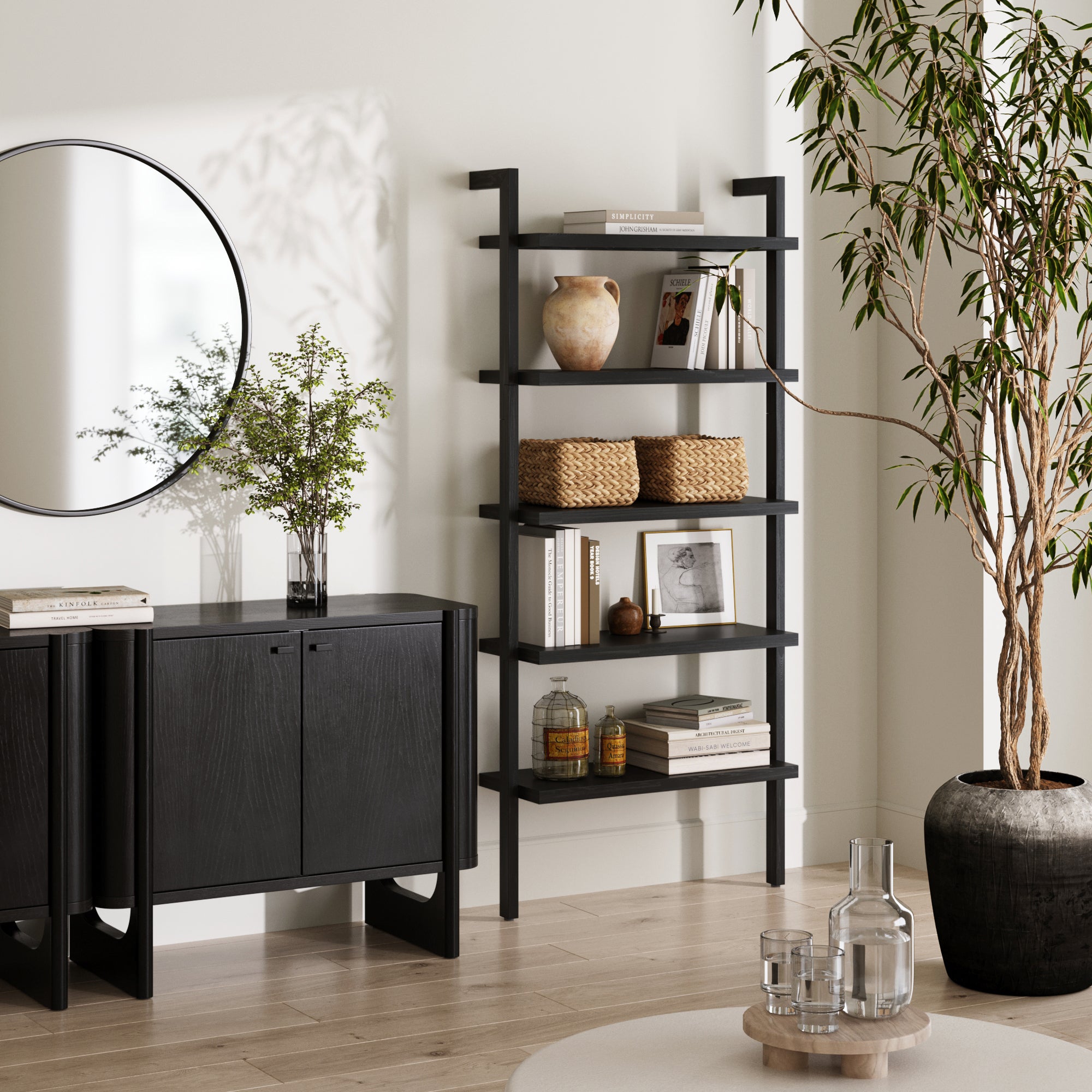 A modern living room with a black sideboard, a round mirror above it, the Nathan James Wood 5 Tier Wall Mounted Bookshelf in Black Oak displaying decor, and a large potted plant on a light wood floor.
