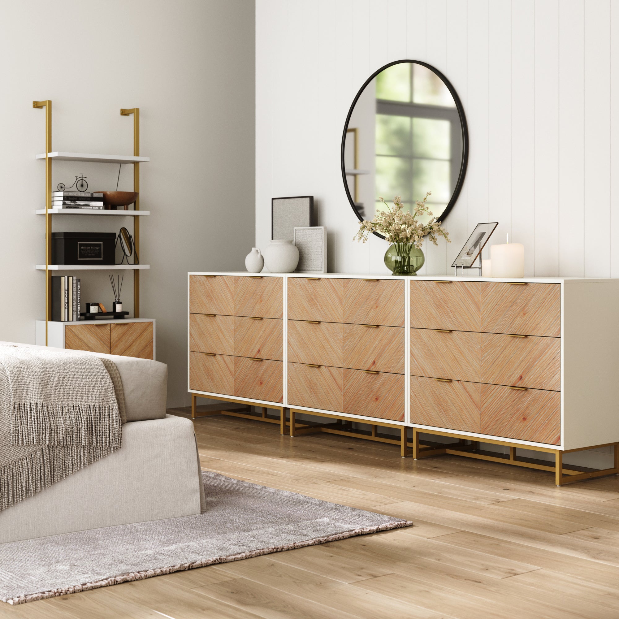 A modern, minimal bedroom features a Nathan James Boho Herringbone 3-Drawer Dresser set in white, a round mirror, decorative vases, and shelving. The bed has a gray throw, with wooden floors and neutral tones completing the look.