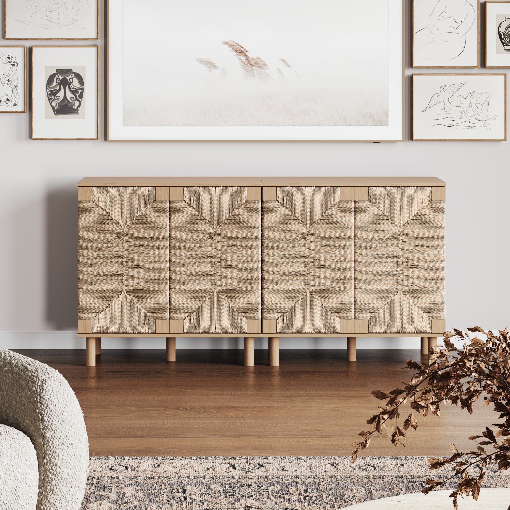 A woven, beige sideboard with geometric patterns stands against a light wall, surrounded by framed artwork and decor. A neutral rug, cozy chair, and dried floral arrangement complete the modern, minimalist living space.