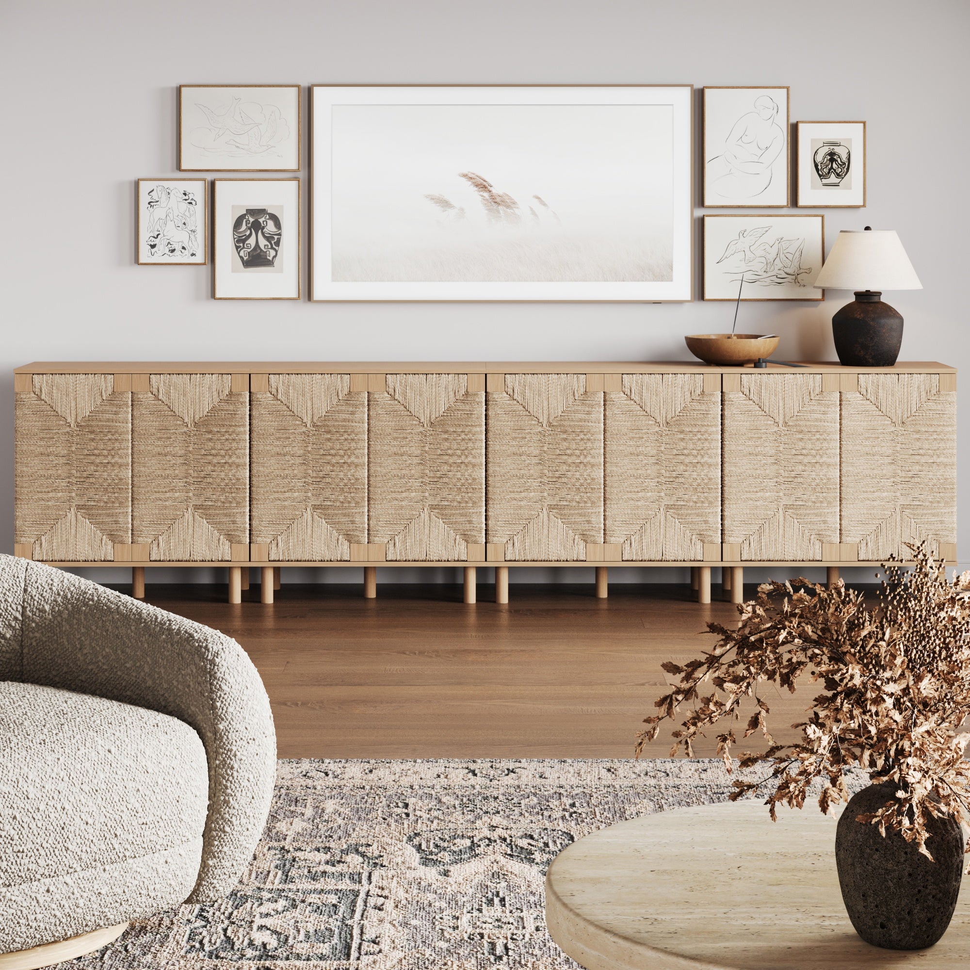 A modern living room with a textured beige sideboard, a neutral armchair, a round table with dried foliage, and a gallery wall of minimal art above the sideboard, featuring a large nature print and smaller sketches.