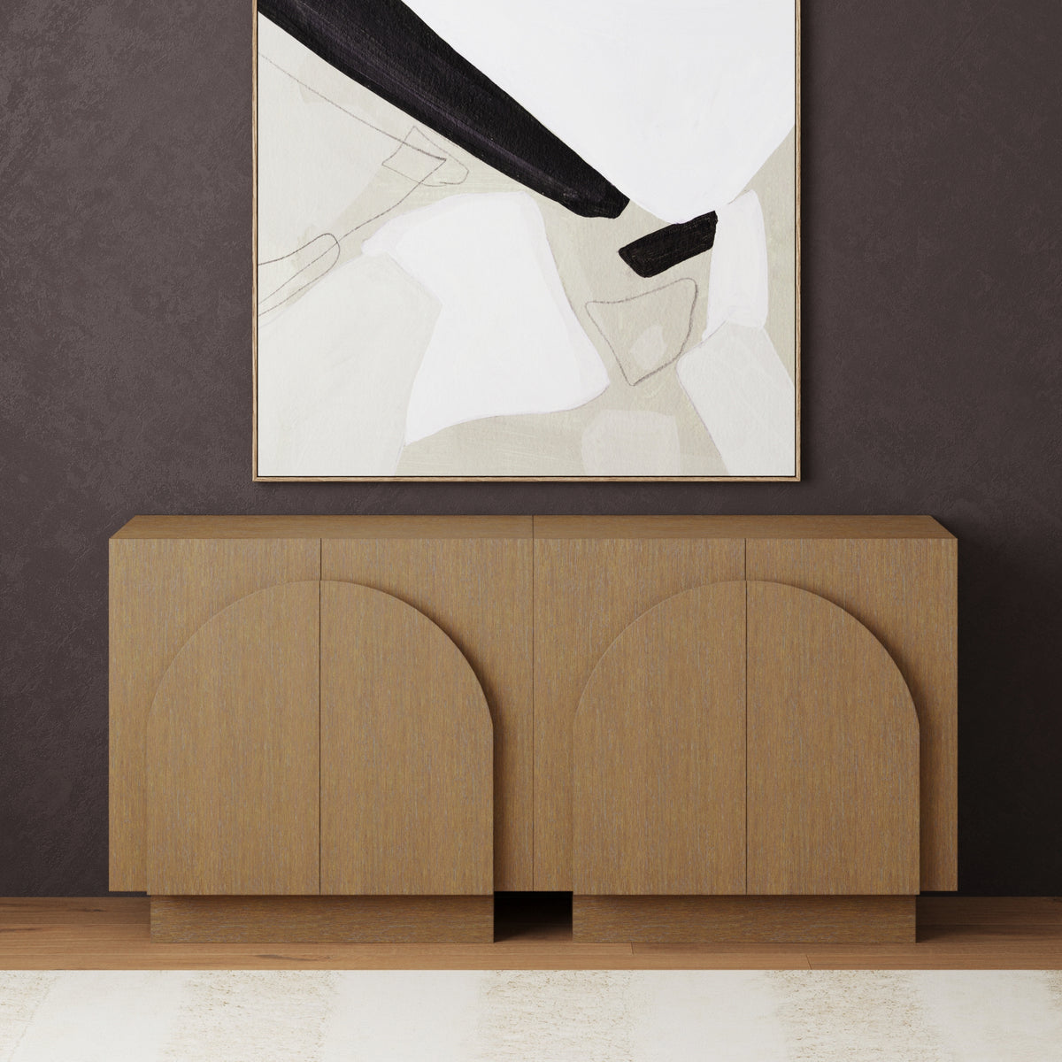 A modern wooden sideboard with arched paneling stands against a dark brown wall, beneath an abstract painting in neutral colors. The floor features wood and a light area rug.
